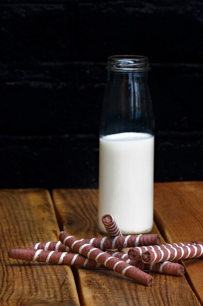 Milk with a cookie in a glass bottle on a wooden background