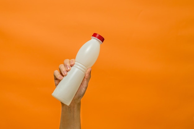 Milk yogurt bottle in man's hand with orange background