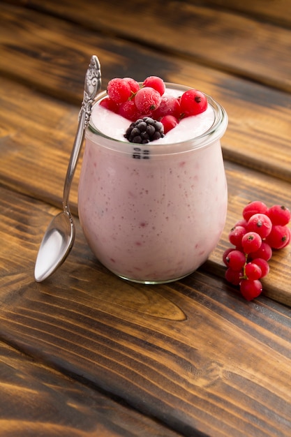 Milk yogurt with berries in the glass jar on the wooden table