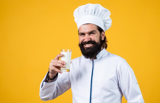 Milkman with milk glass male cook ready for preparing food brutal hipster in apron going to be cooking meal time for eating happy baking concept of housekeeping mature bearded man wear chef hat