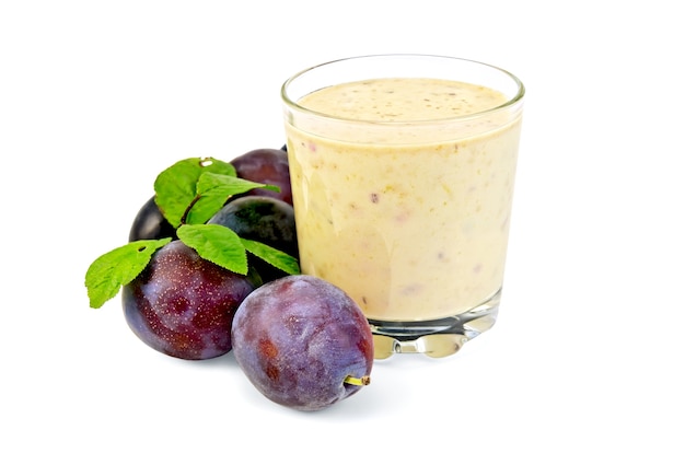 Milkshake in a glass beaker with plums and green leaves it is isolated