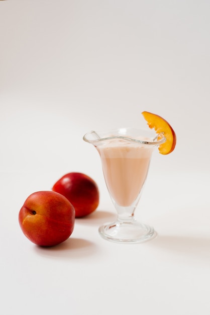 Milkshake met verse nectarines of perziken in een glas op een witte achtergrond, naast perziken of nectarines