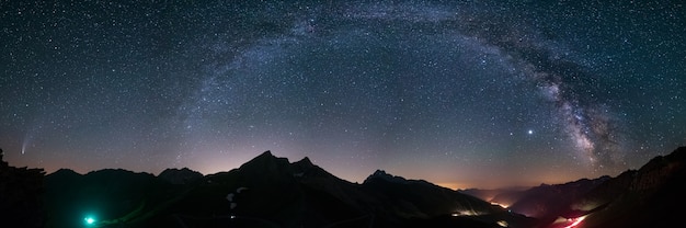 Milky way arc and stars in night sky over the alps. outstanding\
comet neowise glowing at the horizon on the left. panoramic view,\
astro photography, stargazing.