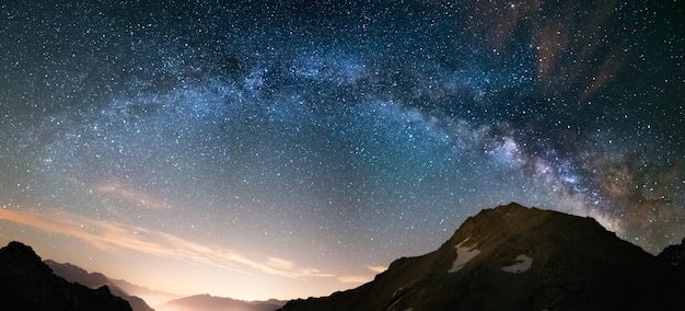 Milky Way arch and starry sky on the Alps. Panoramic view, astro photography, stargazing. Light pollution in the valley below.