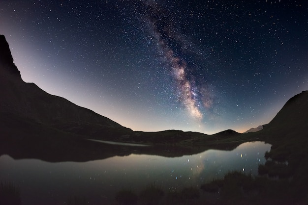 天の川のアーチと星空は、アルプスの標高の高い湖に反映されます。魚眼レンズの景色の歪みと180度のビュー。