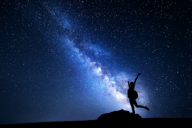 Milky way. night sky with stars and silhouette of a happy woman with backpack and raised up arms. space background