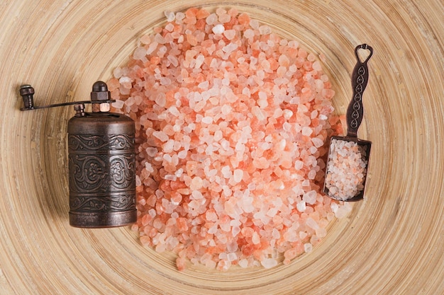 Фото Мельница и ложка специй с рассеянной розовой солью на деревянном фоне.