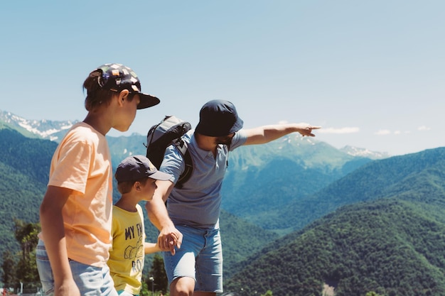 millenial bearded tourist man showing boys high mountains. Travel hiking with children