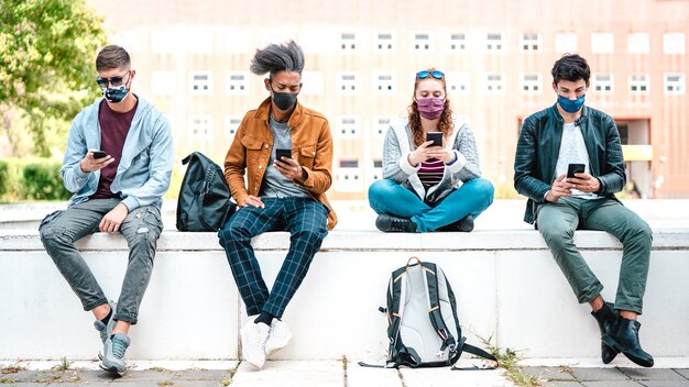 Millenial friends using smart phones with face mask on Covid second wave