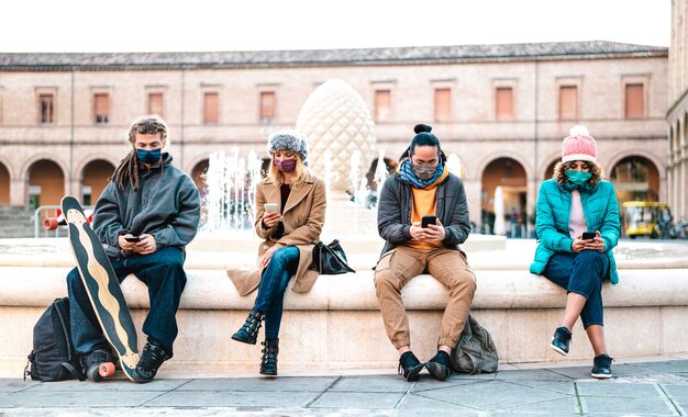 Amici millenari che guardano video su smartphone con maschera facciale sulla seconda ondata di covid