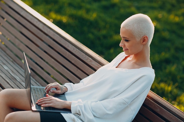 Millenial jonge vrouw blond kort haar buiten lachend portret met laptop