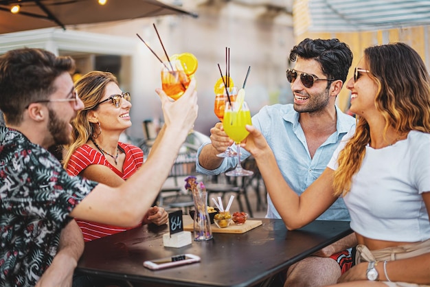 Millenial people on vacation meet at outdoors pub in the summer Group of young friends toasting with fresh cocktail glasses sitting carefree at the pub restaurant alcohol life style concept