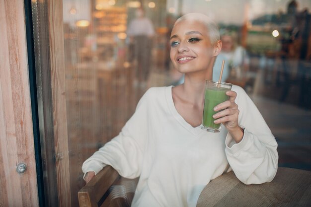 Millenial young woman blonde short hair indoor with green smoothie