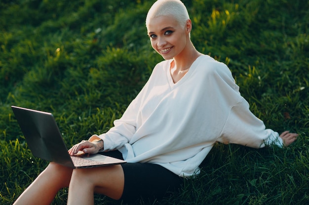 Millenial young woman blonde short hair outdoor smiling portrait with laptop