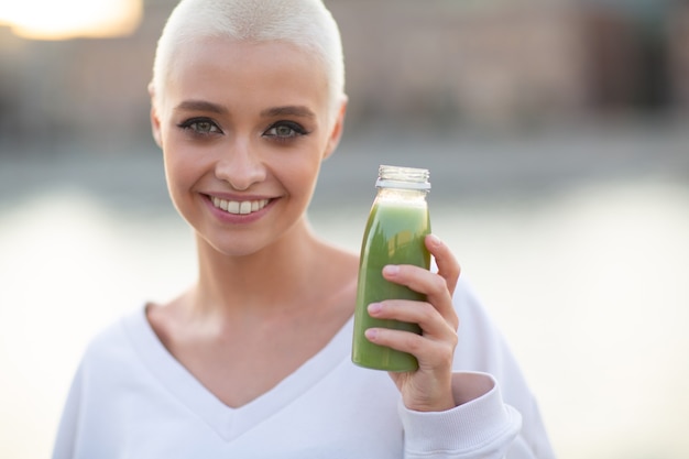 Foto millenial giovane donna bionda capelli corti all'aperto con frullato verde