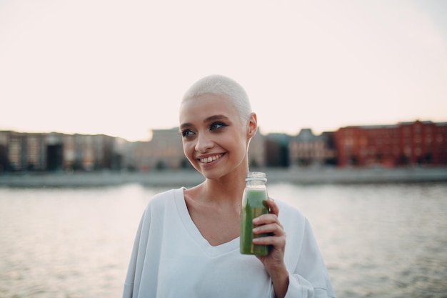 Millenial giovane donna bionda capelli corti all'aperto con frullato verde