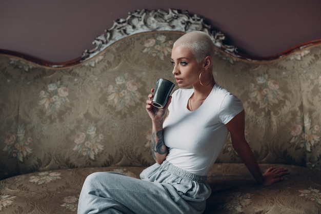 Millenial young woman with short blonde hair portrait sitting on vintage sofa.