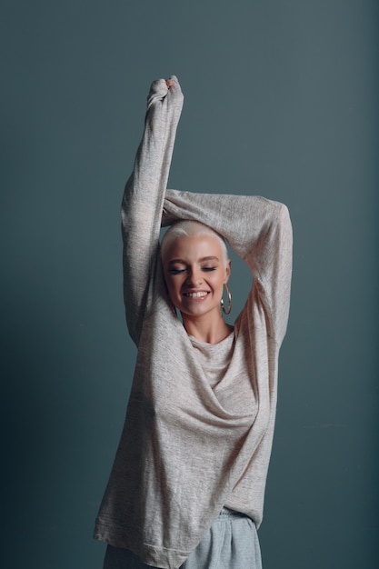 Millenial young woman with short blonde hair portrait with hands up in the air.