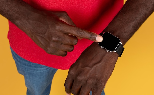 밀레니엄 세대의 아프리카계 미국인 남성 택배사가 빨간색 유니폼을 입고 빈 화면으로 시계를 바라보고 있습니다.