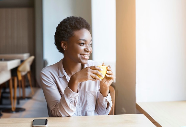 Millennial african lady relaxing with cup of coffee in cafe