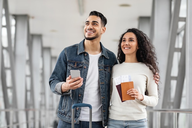 Millennial arab couple standing at airport together and looking away