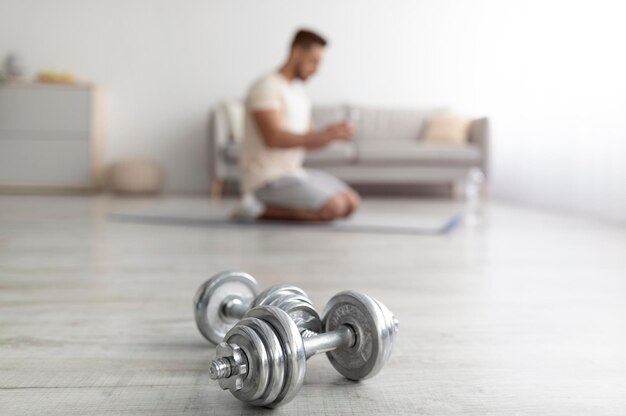 Millennial arab guy exercising at home during covid lockdown selective focus on dumbbells