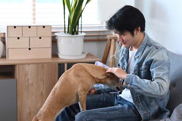 Millennial asian man playing with his adorable dog in living room