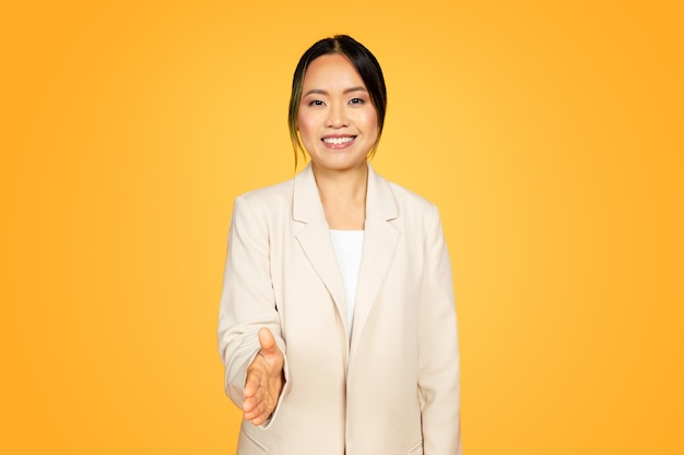 Millennial asian woman in yellow extending hand warmly for a handshake welcoming gesture