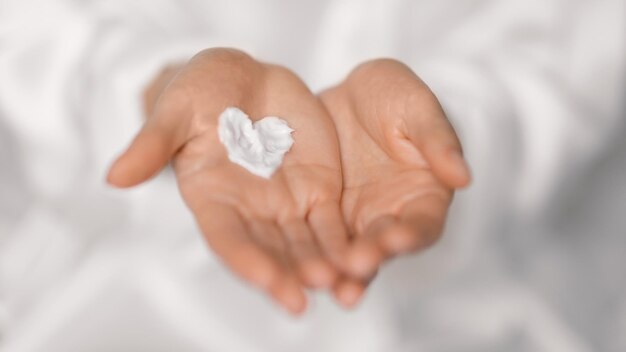Millennial european woman applying cream on heart shaped on hands enjoy daily procedures in bedroom