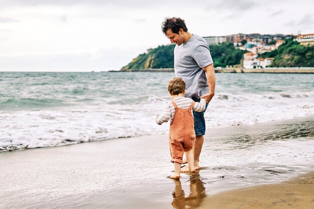 Padre millenario con suo figlio di tre anni che gioca con il ciao in riva al mare