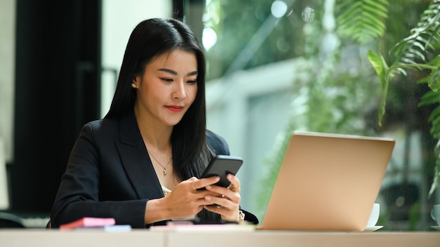 노트북 앞에 앉아 스마트폰을 사용하는 밀레니엄 여성 기업가