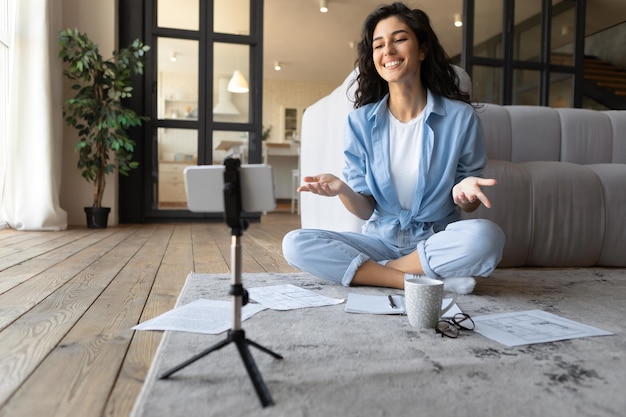 Millennial female teacher conducting online lesson on cellphone\
camera blogger streaming on social media at home