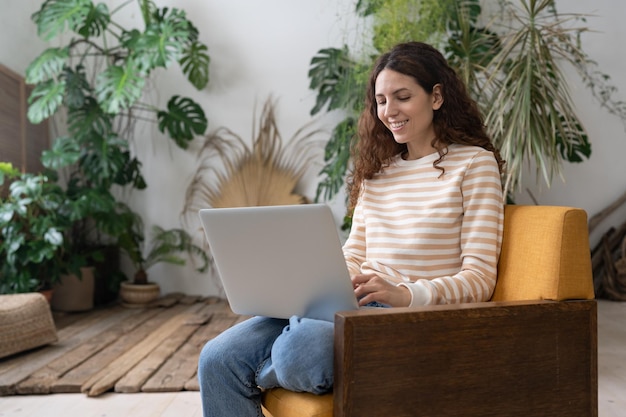 Millennial hispanic woman student studying at college greenhouse using laptop computer on her knees