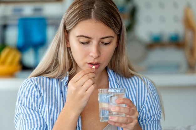 Photo millennial ill sick woman taking painkiller medicine to relieve stomachache pain sit on bed in the morning sick woman lying in bed with high fever cold flu and migraine