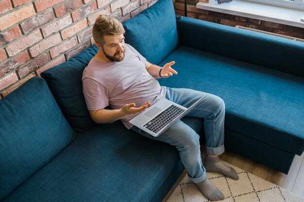 Millennial man at home on couch talking by video call with a laptop technologies for freelancer and
