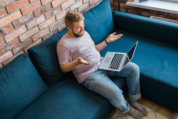 Millennial man at home on couch talking by video call with a laptop technologies for freelancer and