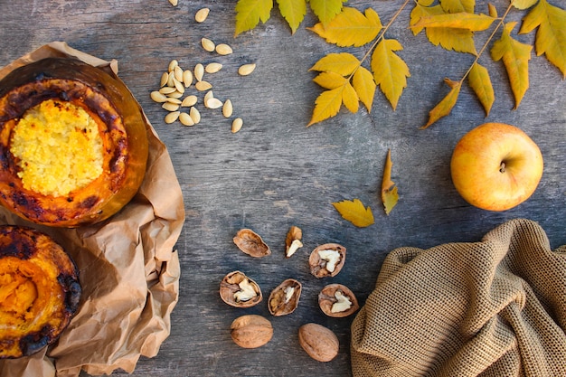 Porridge di miglio cotto in zucca, noci, semi, mela, foglie gialle, maglione caldo su un vecchio legno