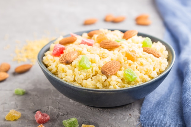 Millet porridge with candied fruits and almonds in blue ceramic bowl on a gray concrete.