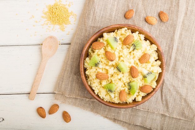 Millet porridge with kiwi and almonds in wooden bowl on a white wooden background. Top view.