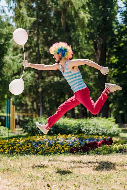 Mime jumps in the park with balloons. 