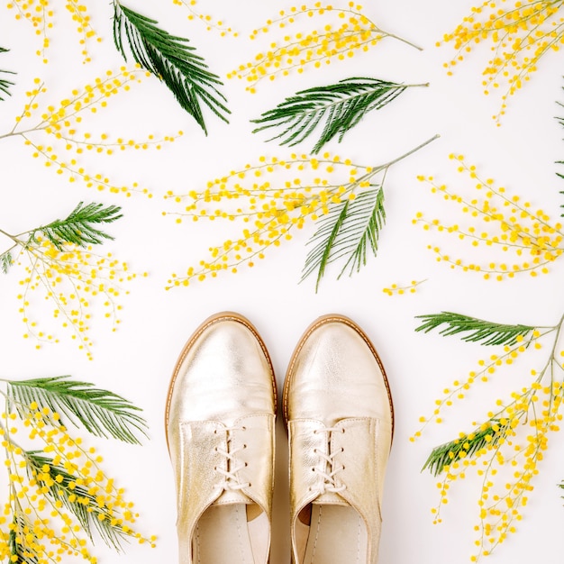 Mimosa flowers and stylish yellow shoes on white background. Flat lay, top view. Spring concept