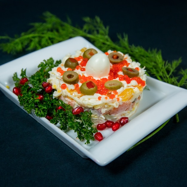 Mimosa salad decorated with herbs in a white plate close up on dark background