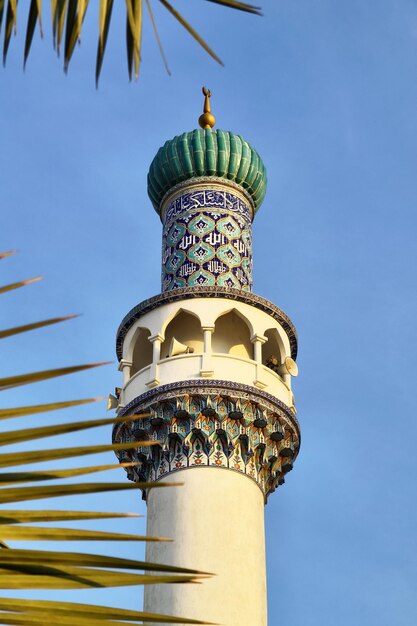 minaret of the mosque against the background of the blue sky is a closeup surrounded by palm leaves