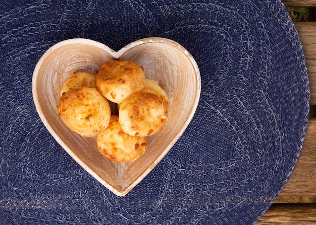 Minas Gerais cheese bread hot on a blue tablecloth top view heart shaped bowl
