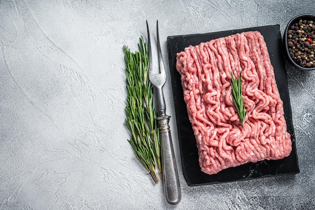 Minced chicken or turkey raw meat on cutting board with herbs. White background. Top View. Copy space.