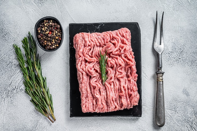 Minced chicken or turkey raw meat on cutting board with herbs. white table. Top View