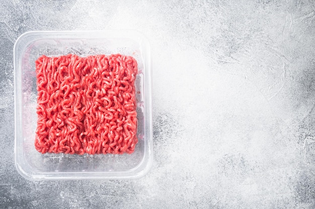 Minced meat in a transparent plastic pack set, on gray stone background, top view flat lay, with copy space for text