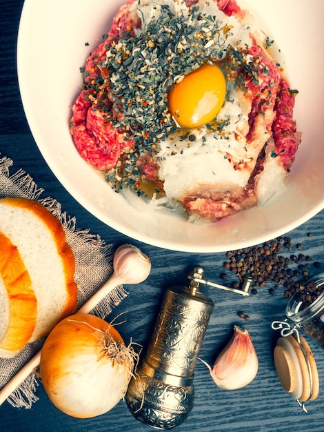 Minced meat with fresh onion garlic herbs on wooden background