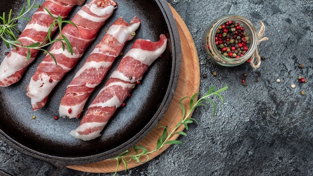 Minced meat wrapped in bacon on cast iron plate. chevapchichi or Kofta kebab. raw sausages of ground beef or pork with onions and spices wrapped in bacon,