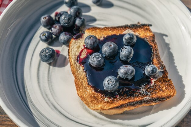 Macinato a vista di un ricco toast di pane con mirtilli freschi e confettura di mirtilli. concetto di colazione sana e naturale.